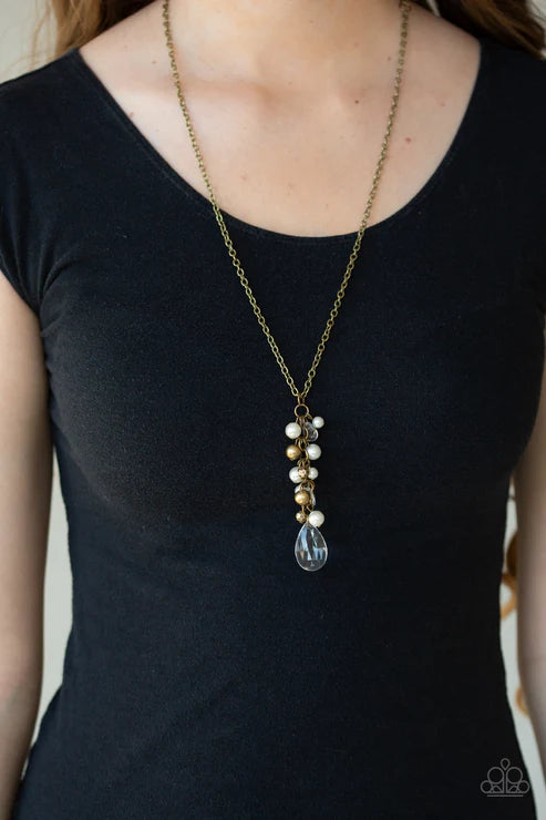 Person wearing a black dress with a long necklace featuring pearls and a teardrop pendant.