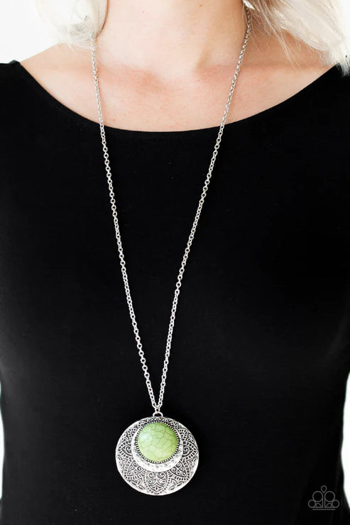 Necklace with a green pendant and silver chain worn by a person against a black background