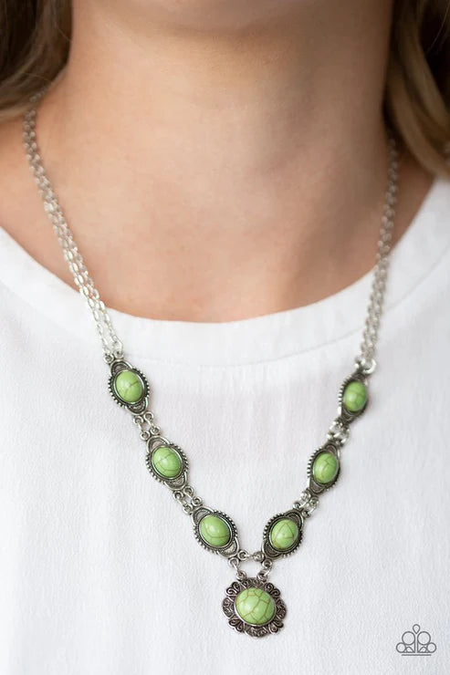 Necklace with green stones and silver chain worn by a person on a white background