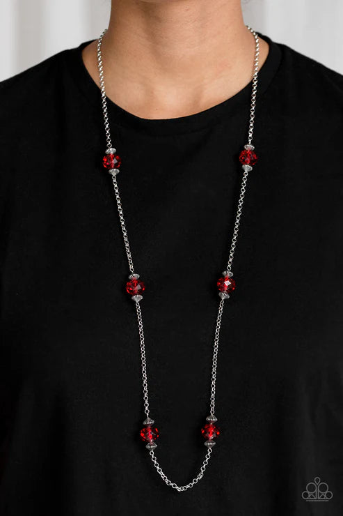Long silver chain necklace with red beads worn by a person on a black shirt.