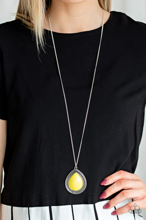 Person wearing a black top with a long necklace featuring a yellow pendant.
