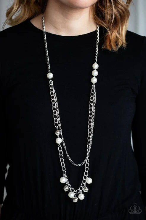 Long necklace with silver chains and white beads worn by a person against a black background