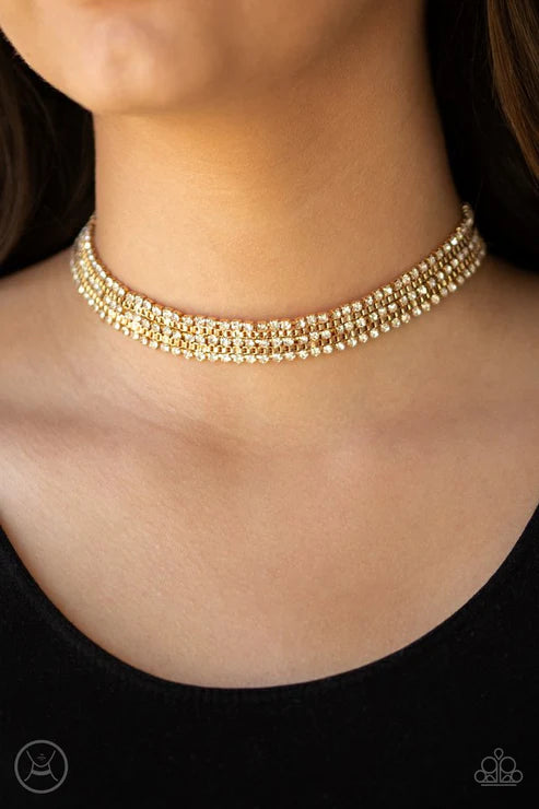 A close-up of a model's neck and upper chest wearing a gold-toned multi-strand rhinestone choker necklace.