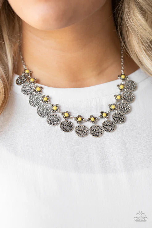 Necklace with circular designs and yellow accents worn by a person on a white background