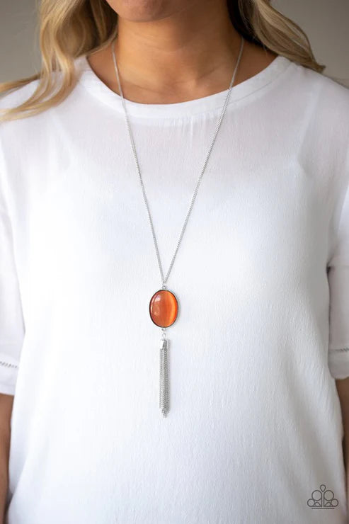Long necklace with a large orange pendant and smaller silver element worn by a person in a white top.