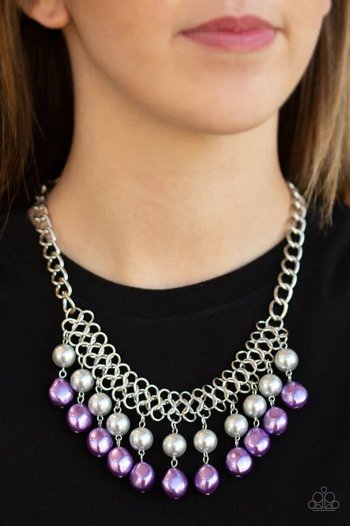 Necklace with purple and silver beads worn by a person against a black background