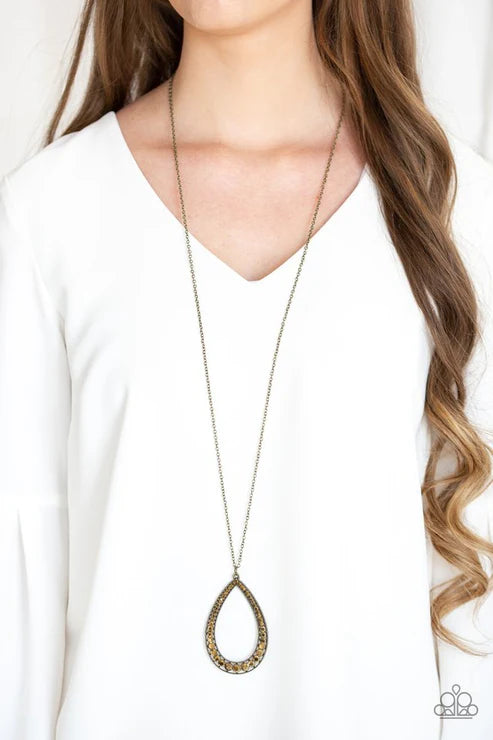 Long necklace with a teardrop pendant worn by a person in a white shirt.