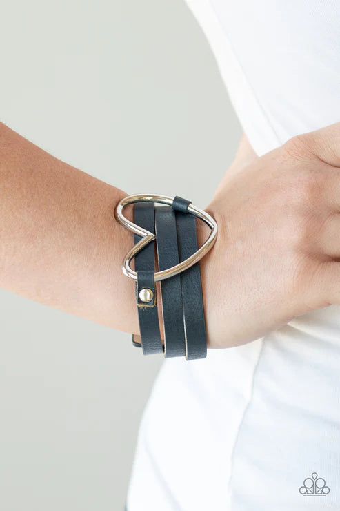 Black leather bracelet with silver heart charm on wrist against a white background