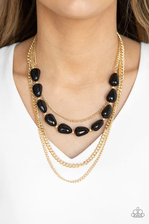 Gold chain necklace with black beads worn by a person on a white background
