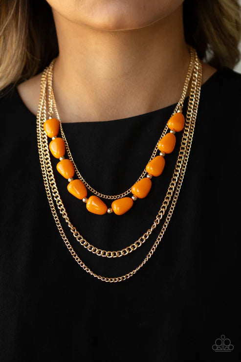 Necklace with orange beads and gold chains on a black background