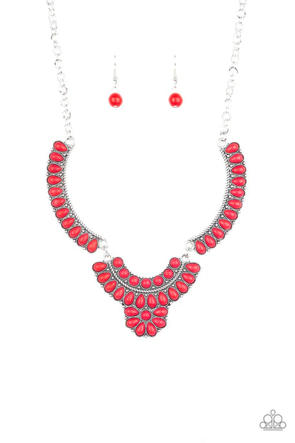 A red and silver statement necklace set with matching drop earrings, featuring a silver-tone chain necklace with a curved collar and V-shaped bib design of red teardrop stones, accompanied by two matching red bead drop earrings on a white background.