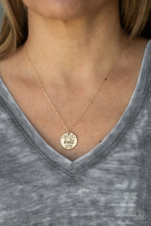 Gold necklace with a pendant worn by a person in a gray shirt