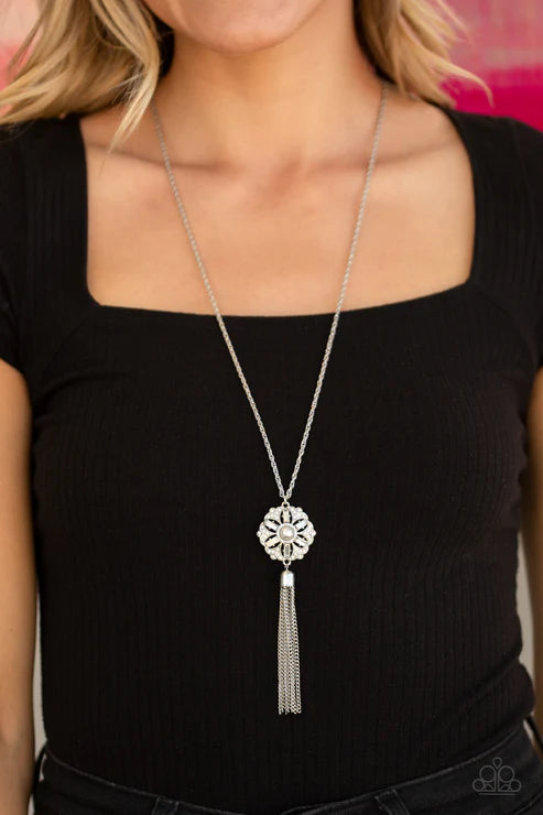 Long silver necklace with a tassel pendant worn by a person in a black top.