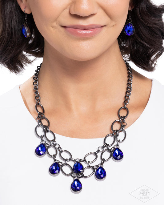Woman wearing a black chain necklace with blue teardrop pendants on a white background
