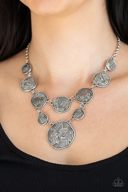 Silver necklace with geometric designs on a person wearing a black top.