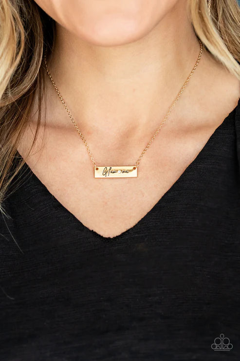 Gold necklace with a bar pendant on a person wearing a black top