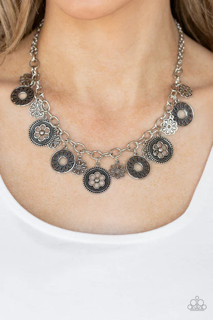 Necklace with floral and circular charms on a person wearing a white shirt.