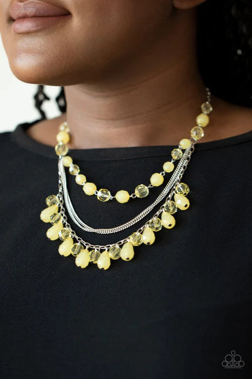 Necklace with yellow beads and silver chain worn by a person against a black background