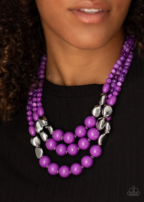 Purple beaded necklace with silver accents worn by a person against a black background