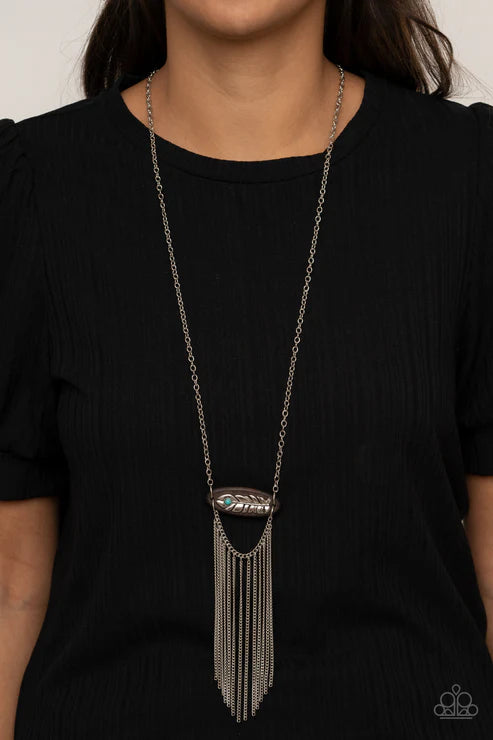 Long silver fringe necklace worn by a person in a black outfit against a neutral background