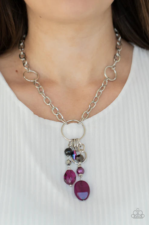 Silver chain necklace with purple and black beads worn by a person on a white background