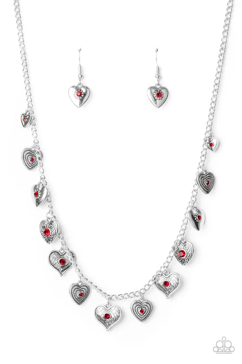 Silver heart-shaped jewelry set with red stones on a white background