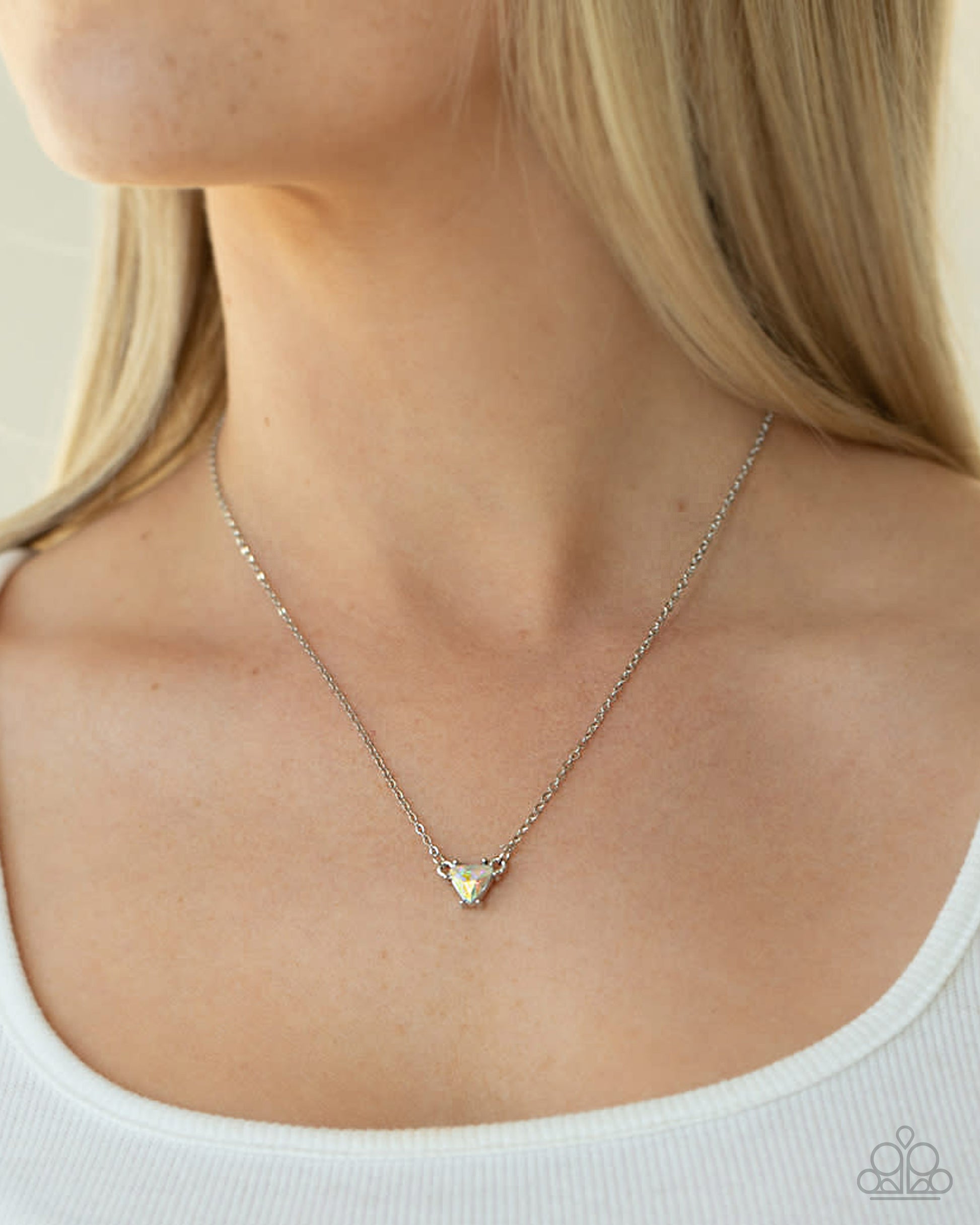 A close-up of a model wearing a delicate silver chain necklace with a small triangular pendant, paired with a white ribbed tank top.