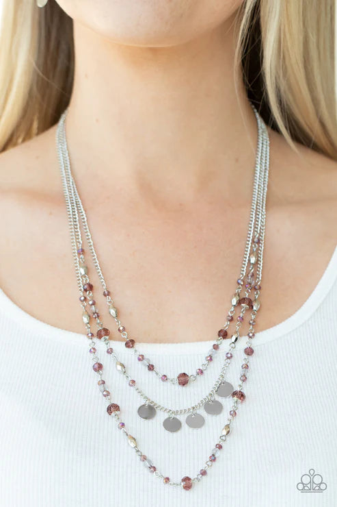 Layered necklace with purple and silver beads on a person wearing a white top.