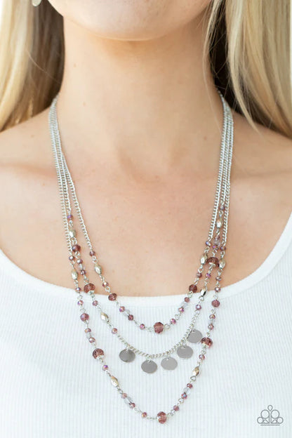Layered necklace with purple and silver beads on a person wearing a white top.