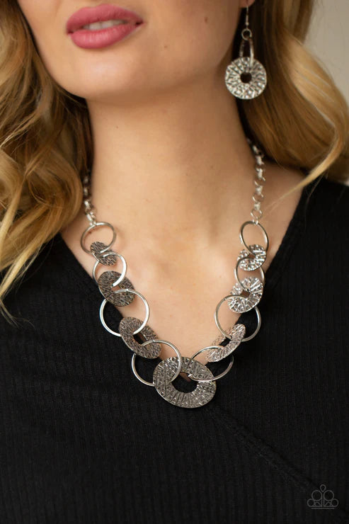 Silver chain necklace and earrings on a person wearing a black top.
