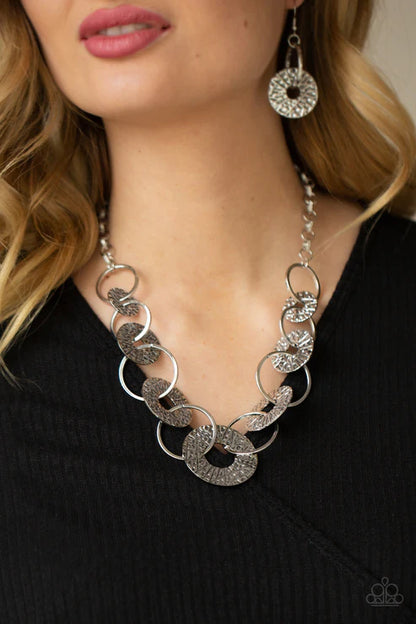 Silver chain necklace and earrings on a person wearing a black top.