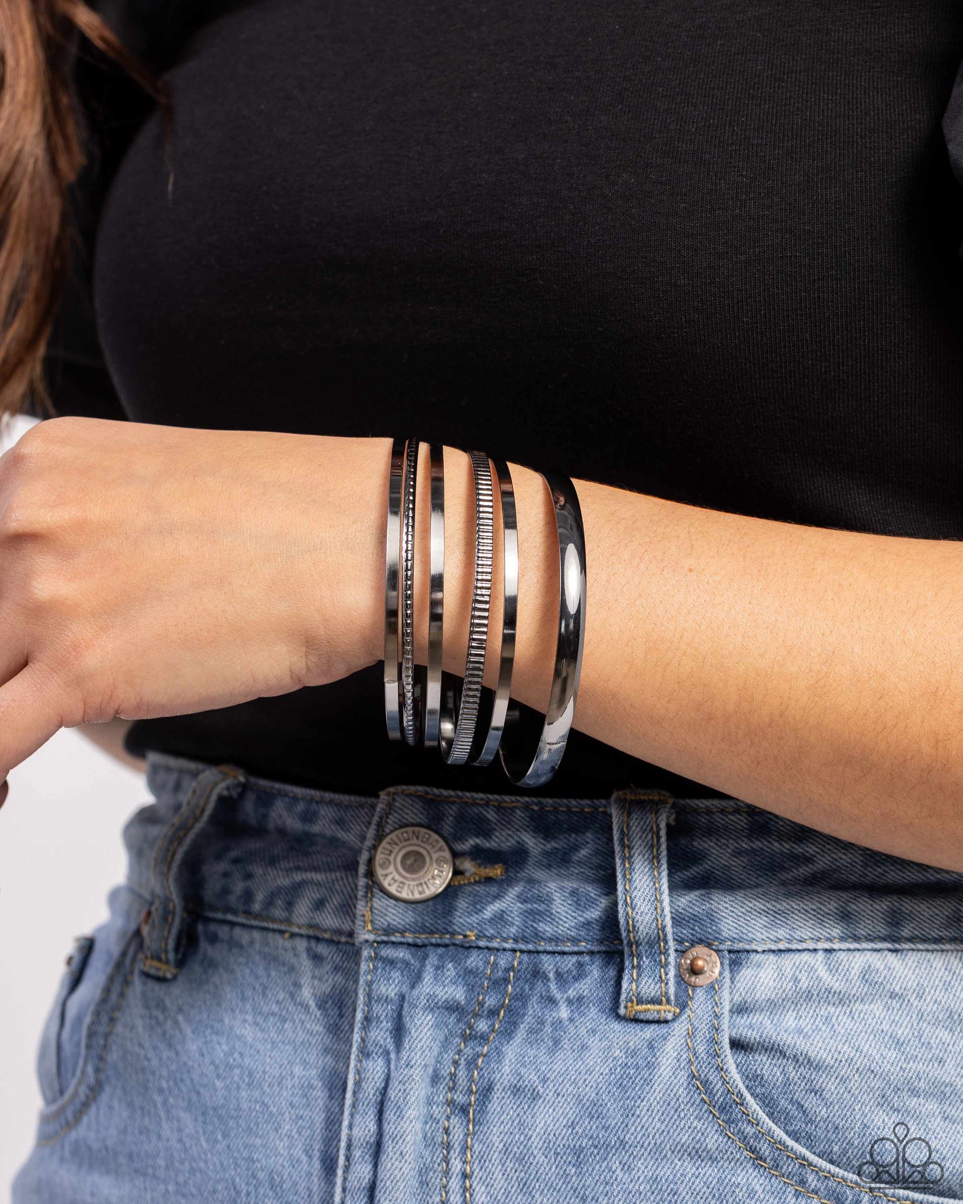 Person wearing multiple silver bracelets on a plain background