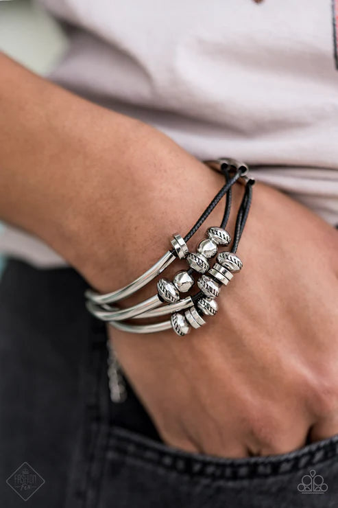Close-up of a wrist wearing multiple silver bracelets on a blurred background
