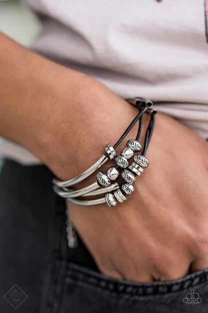 Close-up of a wrist wearing multiple silver bracelets on a blurred background