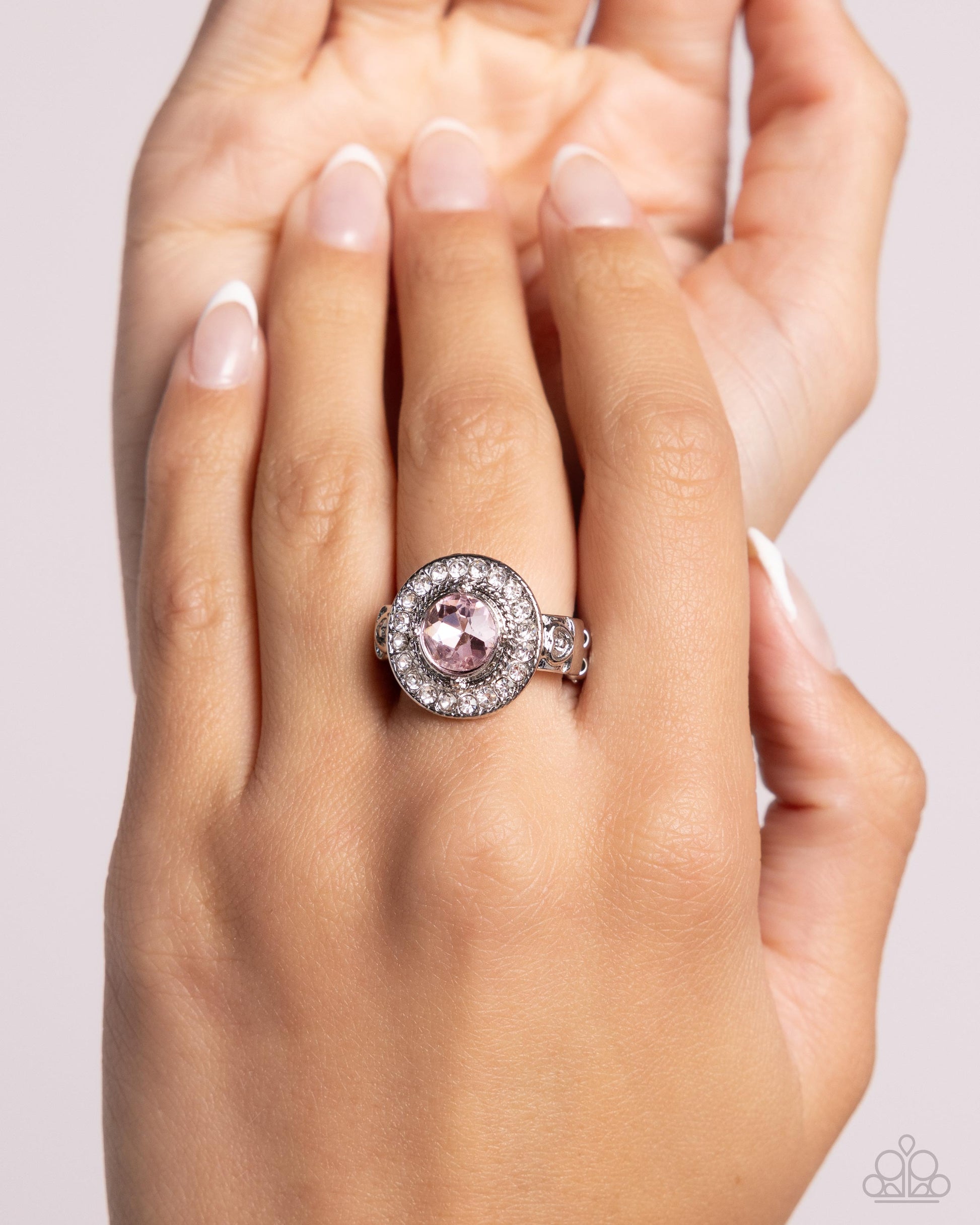 Hand wearing a ring with a pink gemstone on a light background