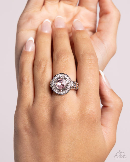 Hand wearing a ring with a pink gemstone on a light background