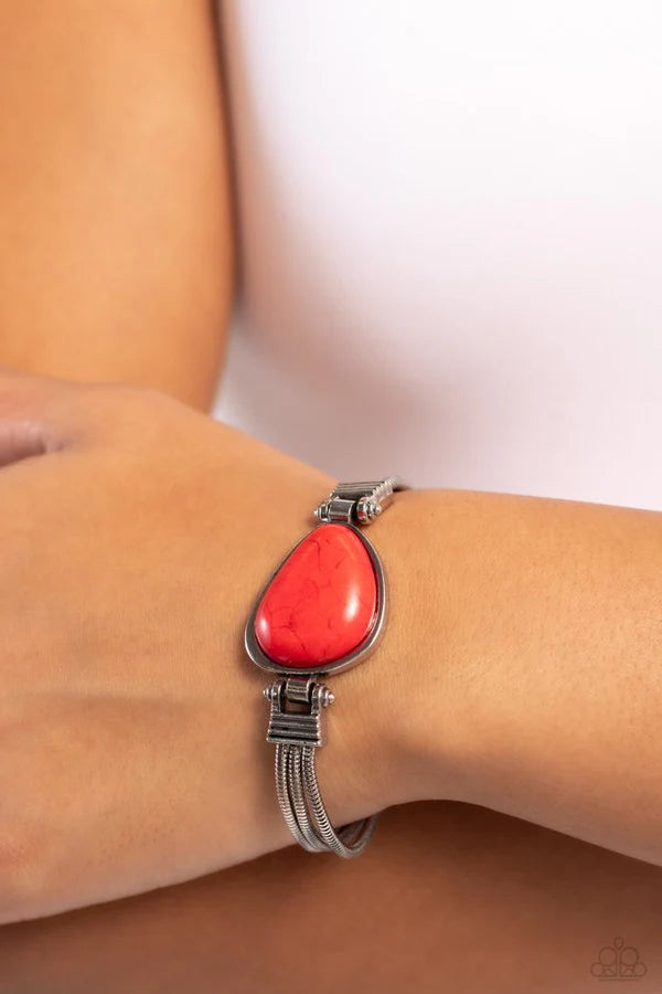 Bracelet with a red stone on a wrist against a neutral background