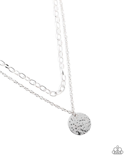 Silver necklace with a round, textured pendant on a white background