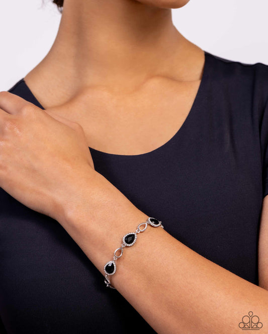 Silver bracelet with black stones on a wrist against a dark background