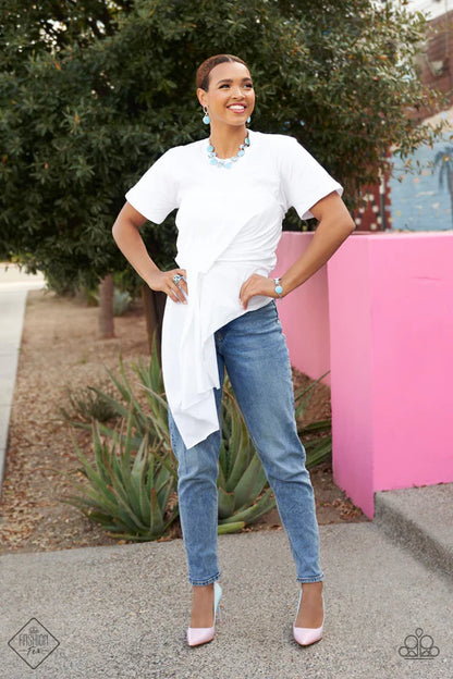 Woman wearing a white top and blue jeans standing outdoors with a pink structure in the background