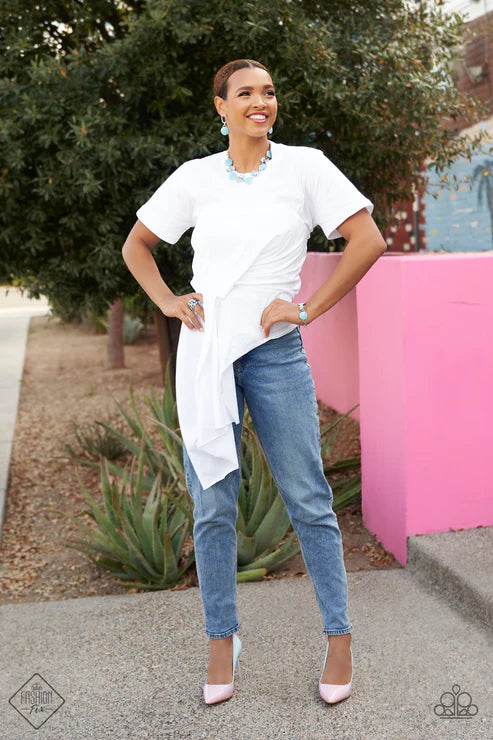 Woman wearing a white top and blue jeans standing outdoors with a pink structure in the background