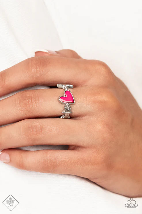 Hand wearing a silver ring with a pink heart design on a white background