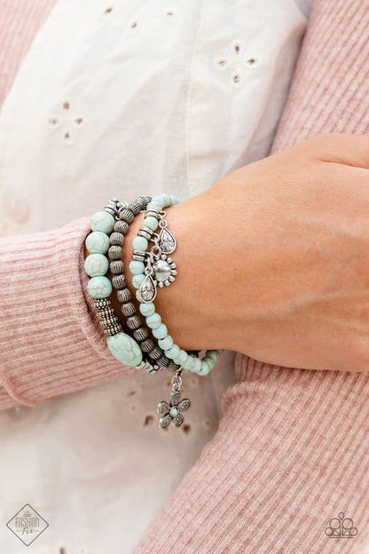 Close-up of a wrist wearing multiple turquoise beaded bracelets with charms on a light pink sweater.