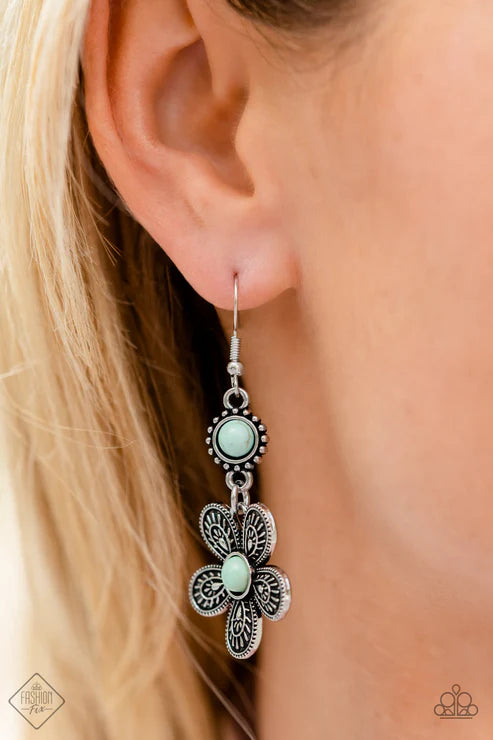 Close-up of an ear wearing a silver floral earring with turquoise stones.