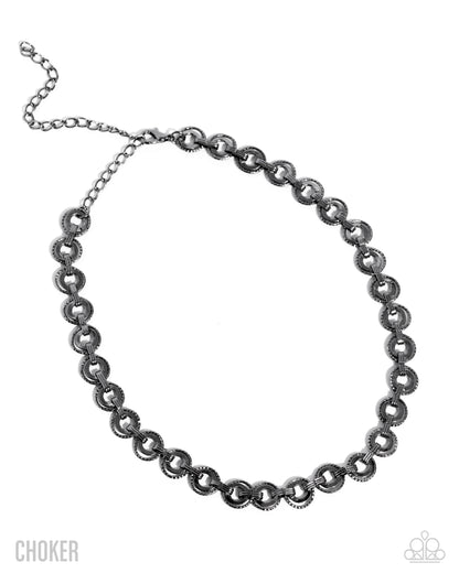 A dark gunmetal silver choker necklace with textured circular links, displayed on a clean white background with a 'CHOKER' text overlay on the bottom left.