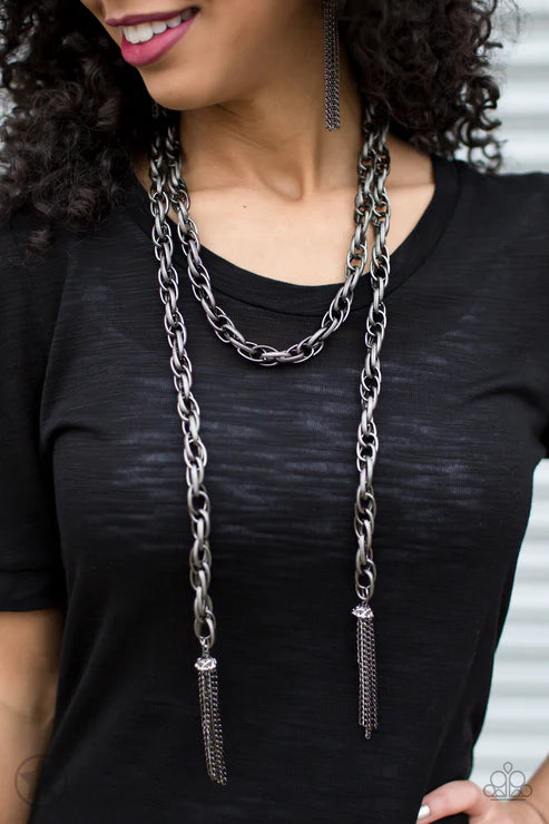 Woman wearing a long chain necklace with a black top.