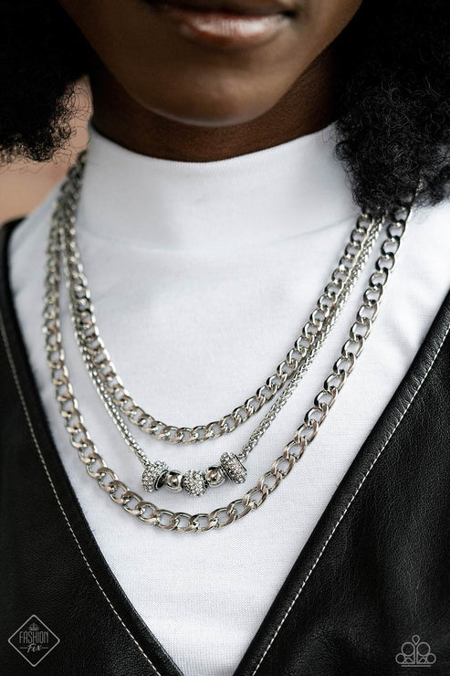 Person wearing multiple silver chain necklaces with a black leather jacket and white shirt.