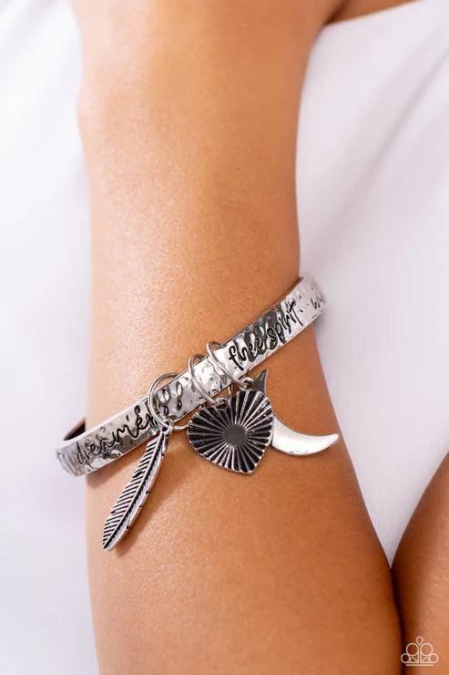 Silver bracelet with feather and sunburst charm on a wrist against a white background