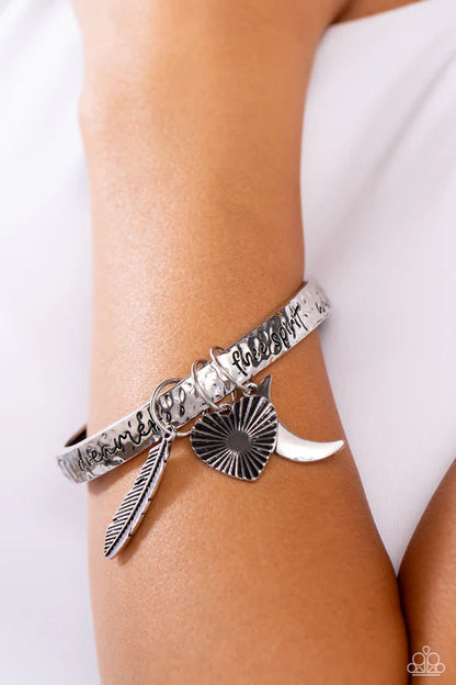 Silver bracelet with feather and sunburst charm on a wrist against a white background
