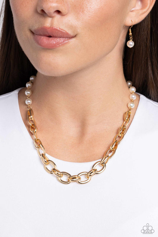Gold chain necklace with pearl accents worn by a model against a white background